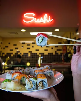 A selection of sushi in front of a neon sushi sign